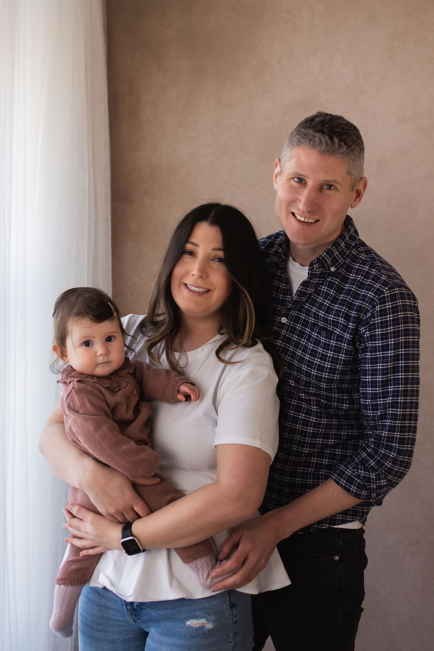 A smiling couple holds their baby daughter in a warm and natural studio family portrait.