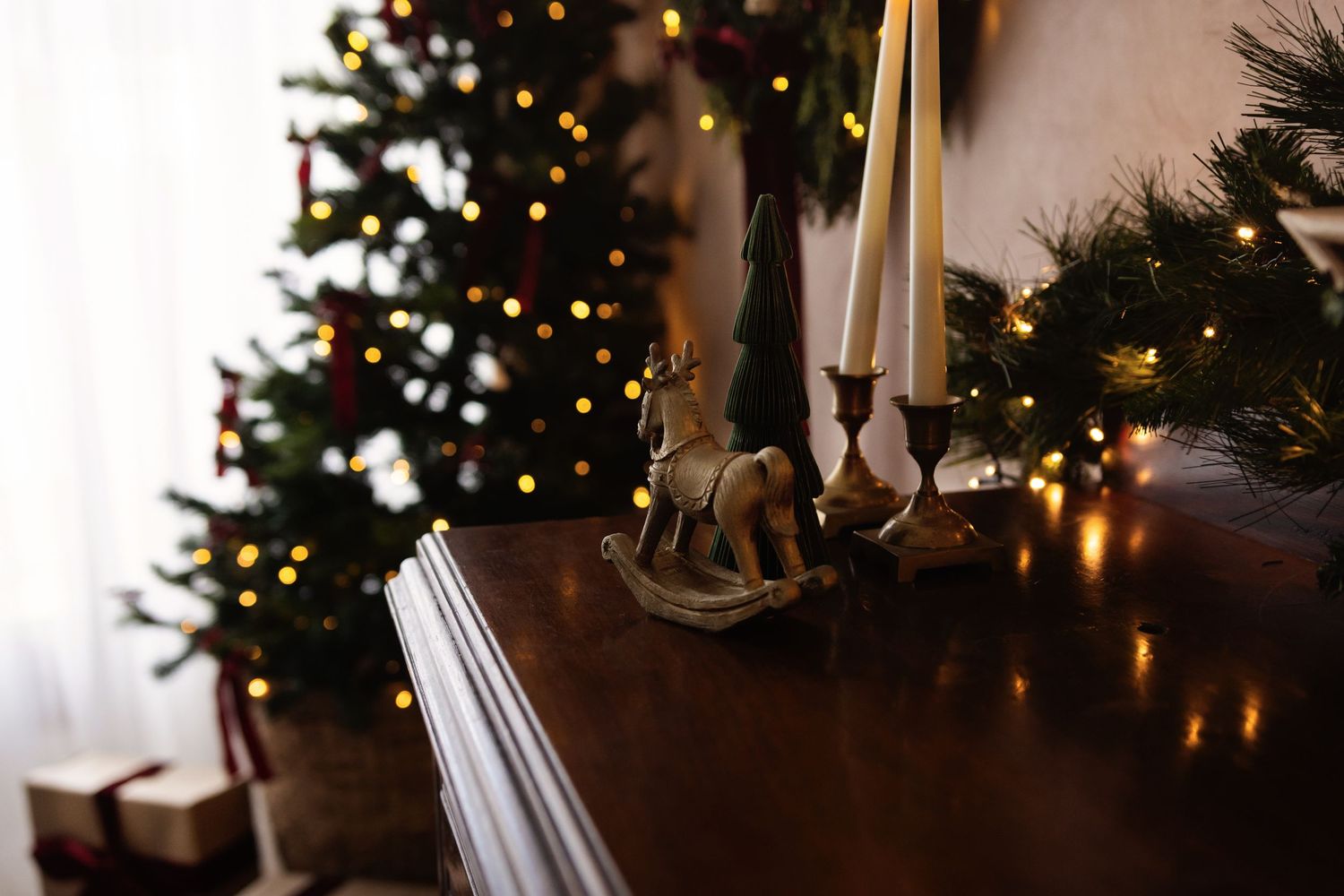Festive Christmas scene with decorated tree, candles, and a wooden rocking horse figurine on a polished wooden surface.