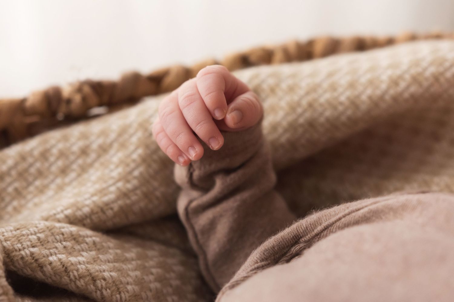 Close-up of newborn baby hand with tiny fingers resting on brown knit fabric in basket.