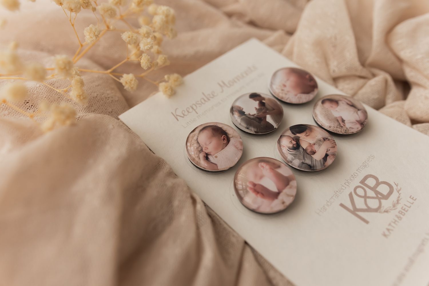 Six round photo keepsake magnets with soft pink tones displayed on a branded card, surrounded by delicate dried flowers.