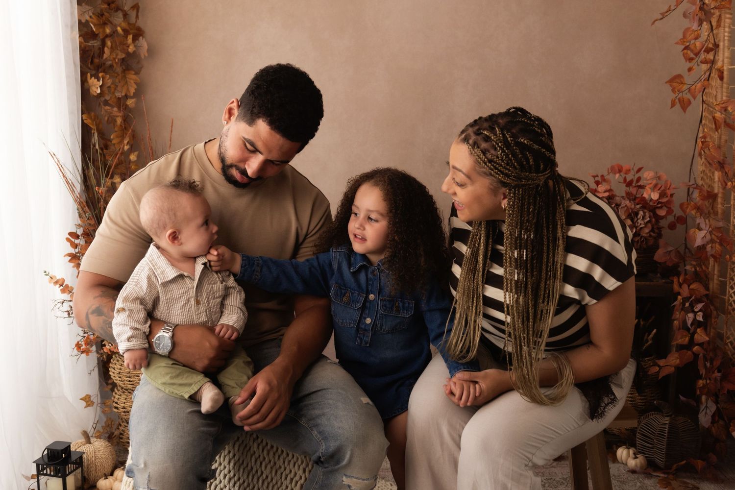 A warm family portrait featuring parents and two children in an autumn-themed studio setting with fall foliage decor.