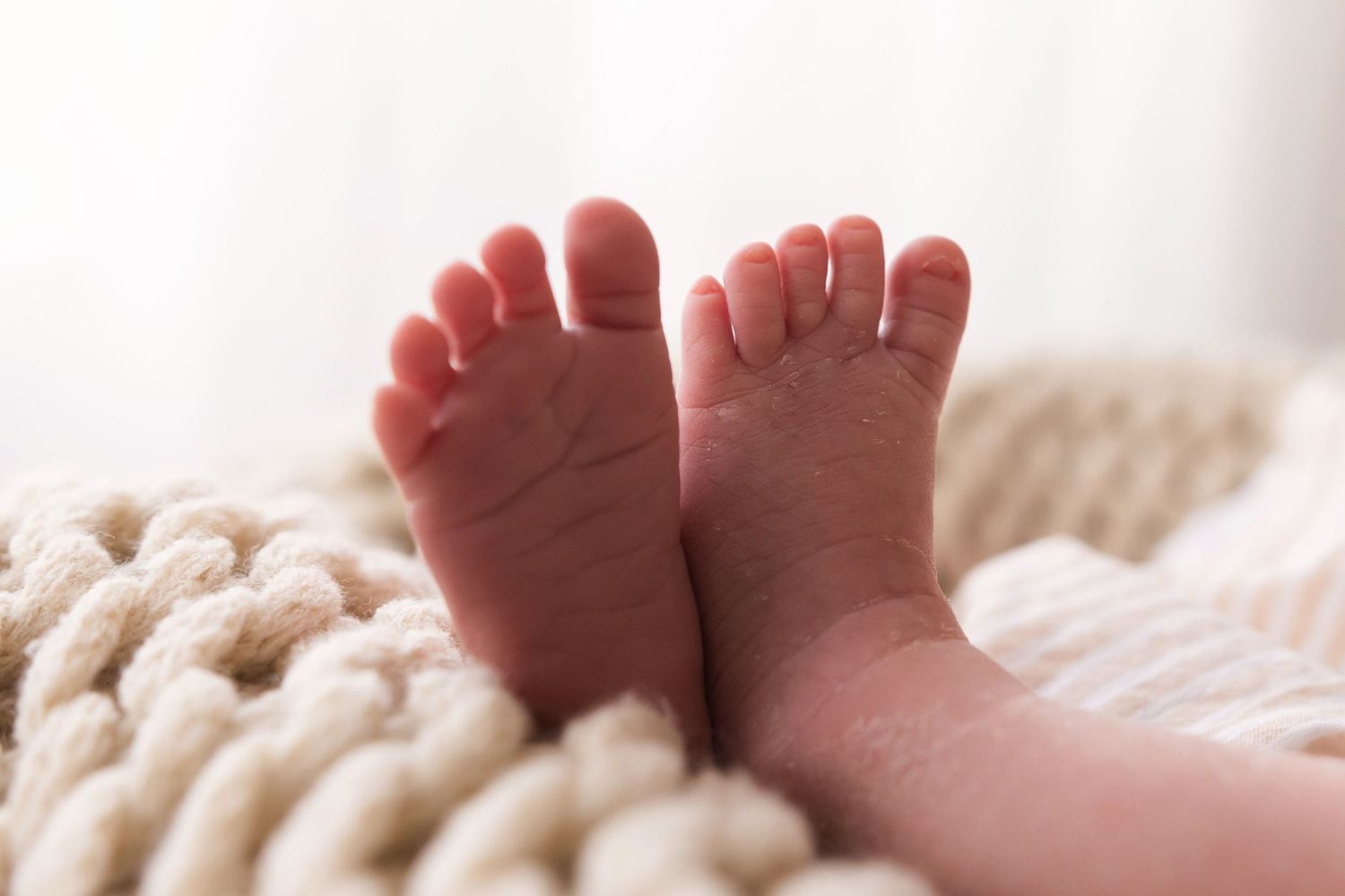 Close-up of tiny newborn baby feet resting on a cream chunky knit blanket.