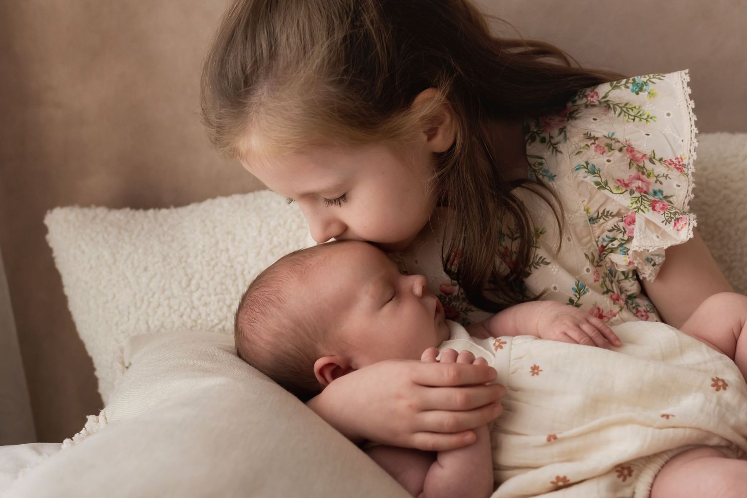 Young girl kissing newborn baby sibling on the head tenderly.