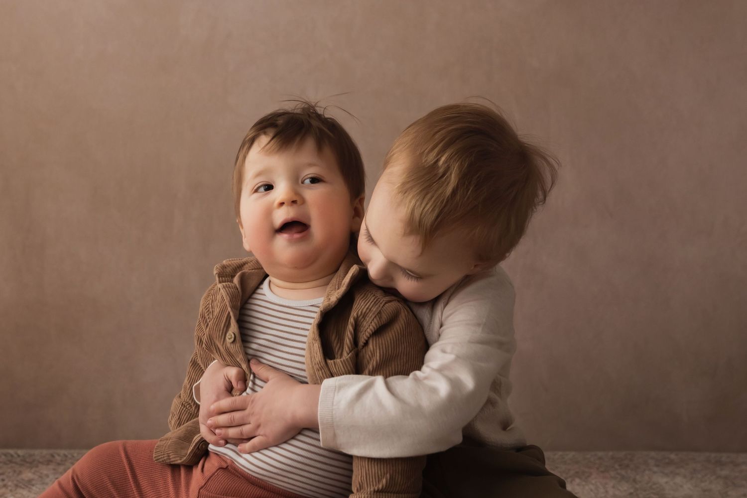 Two babies share a sweet moment, one laughing joyfully as the other gives a gentle kiss on the cheek.