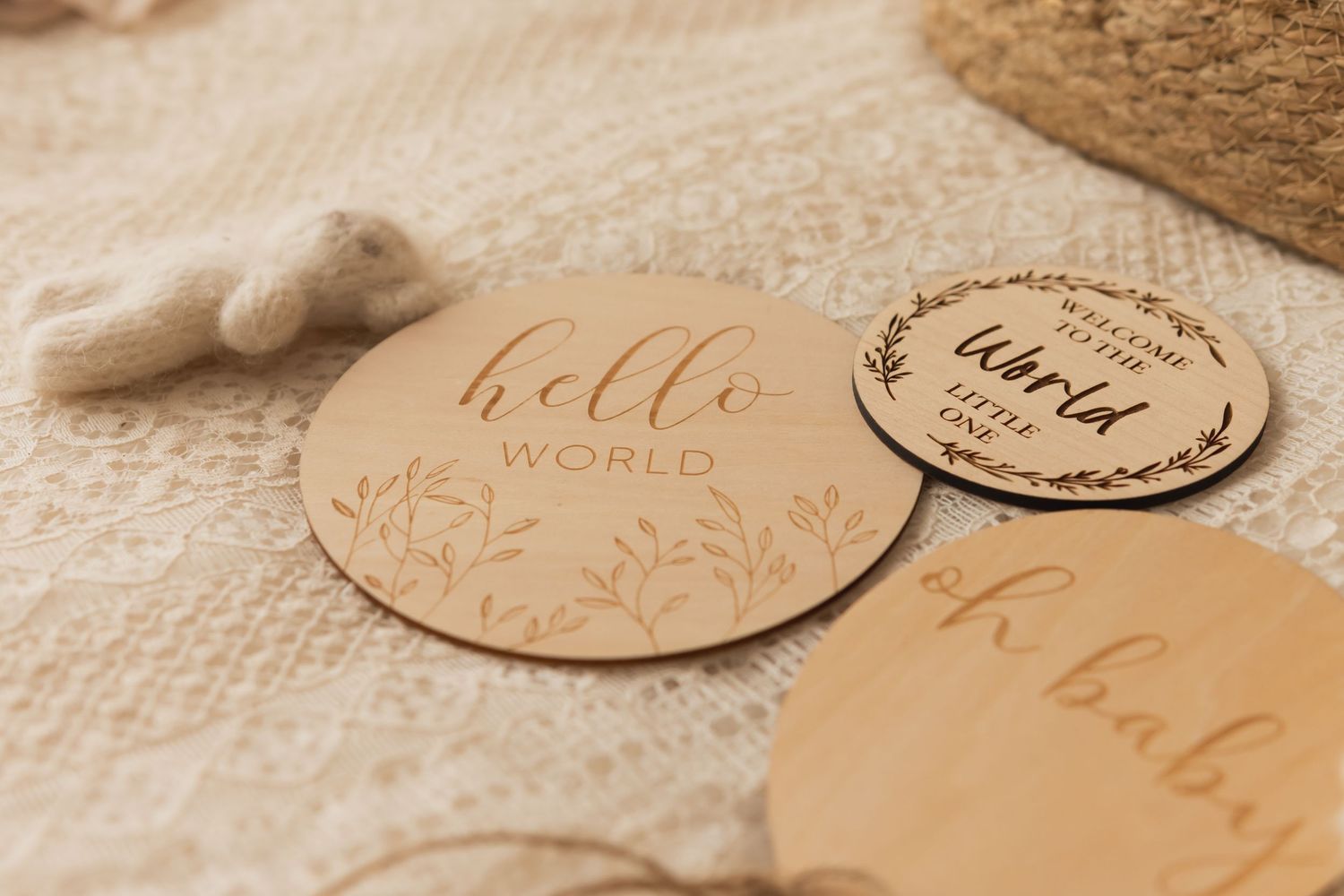 Wooden baby milestone discs with Hello World engravings, arranged on a soft textured blanket with decorative elements.