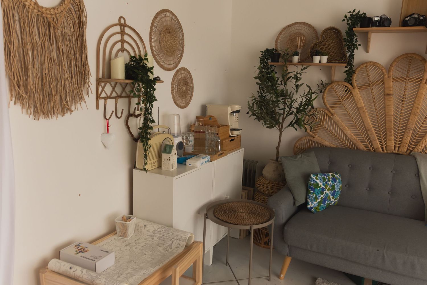 Bohemian living room with rattan wall decor, gray sofa, woven baskets, and a small potted olive tree.