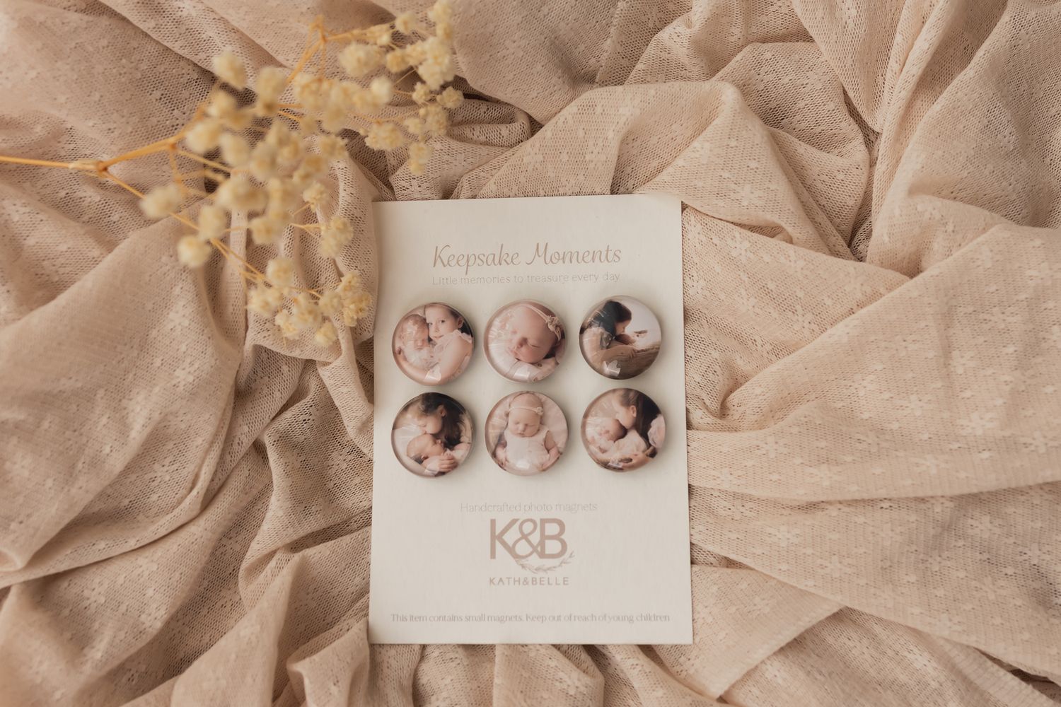 Six round photo buttons displayed on a K&B Keepsake Memories card, arranged on beige fabric with dried flowers.