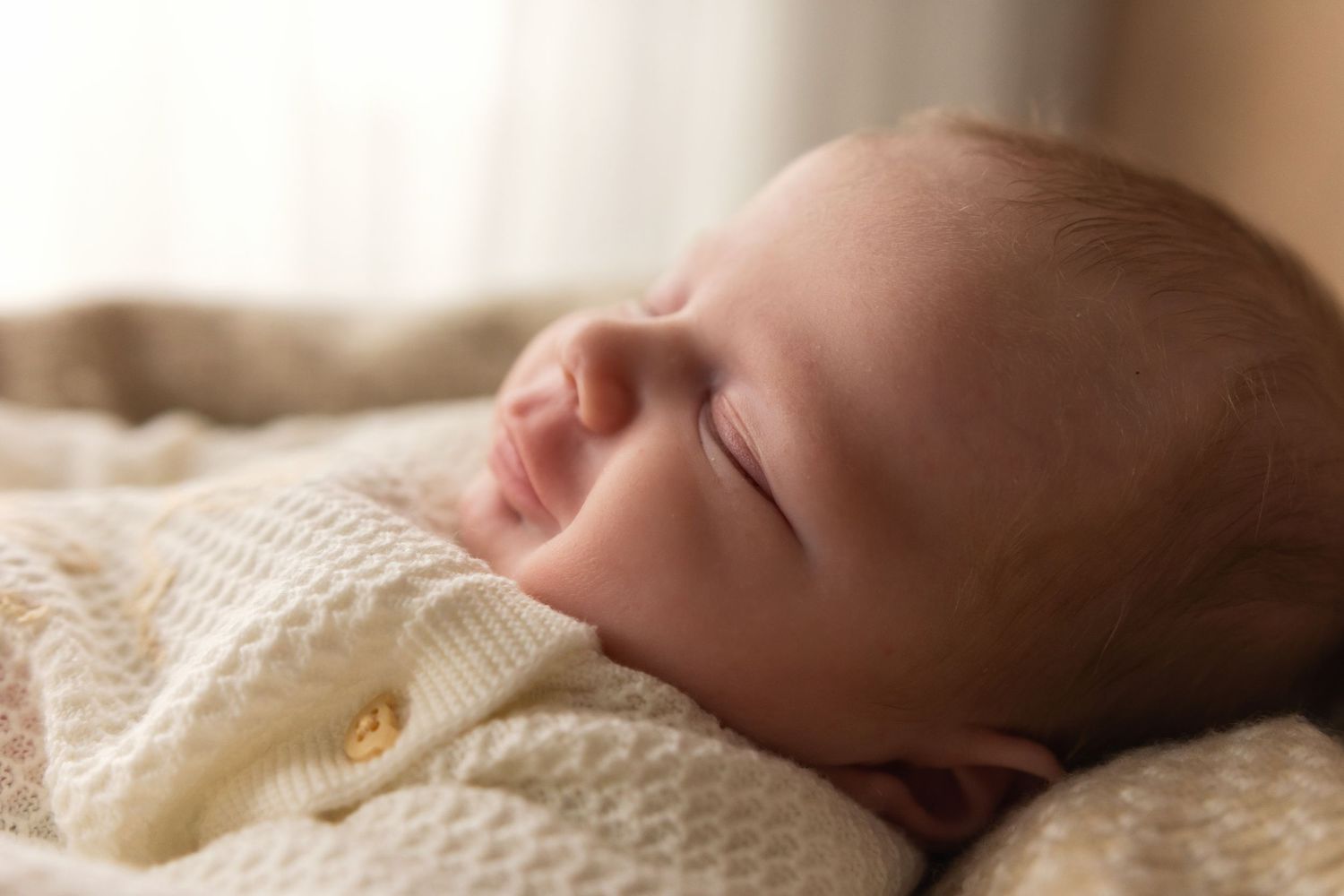 Peaceful sleeping newborn baby in cream knit outfit resting on soft blanket.