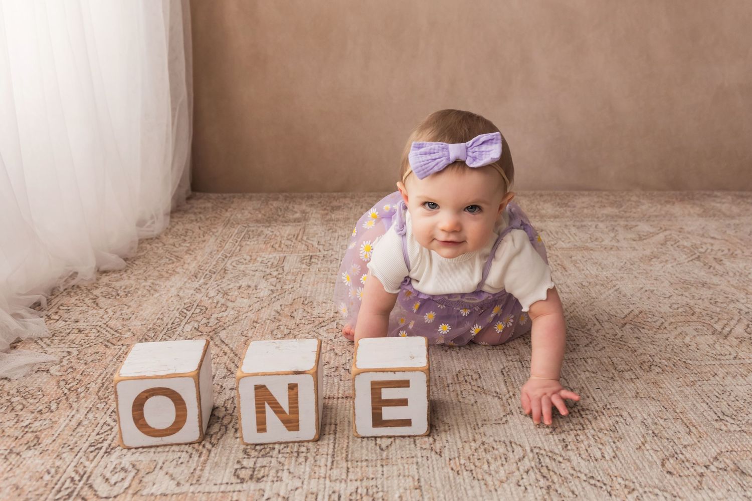 Baby girl in purple tutu crawling near wooden ONE blocks for first birthday photo session.