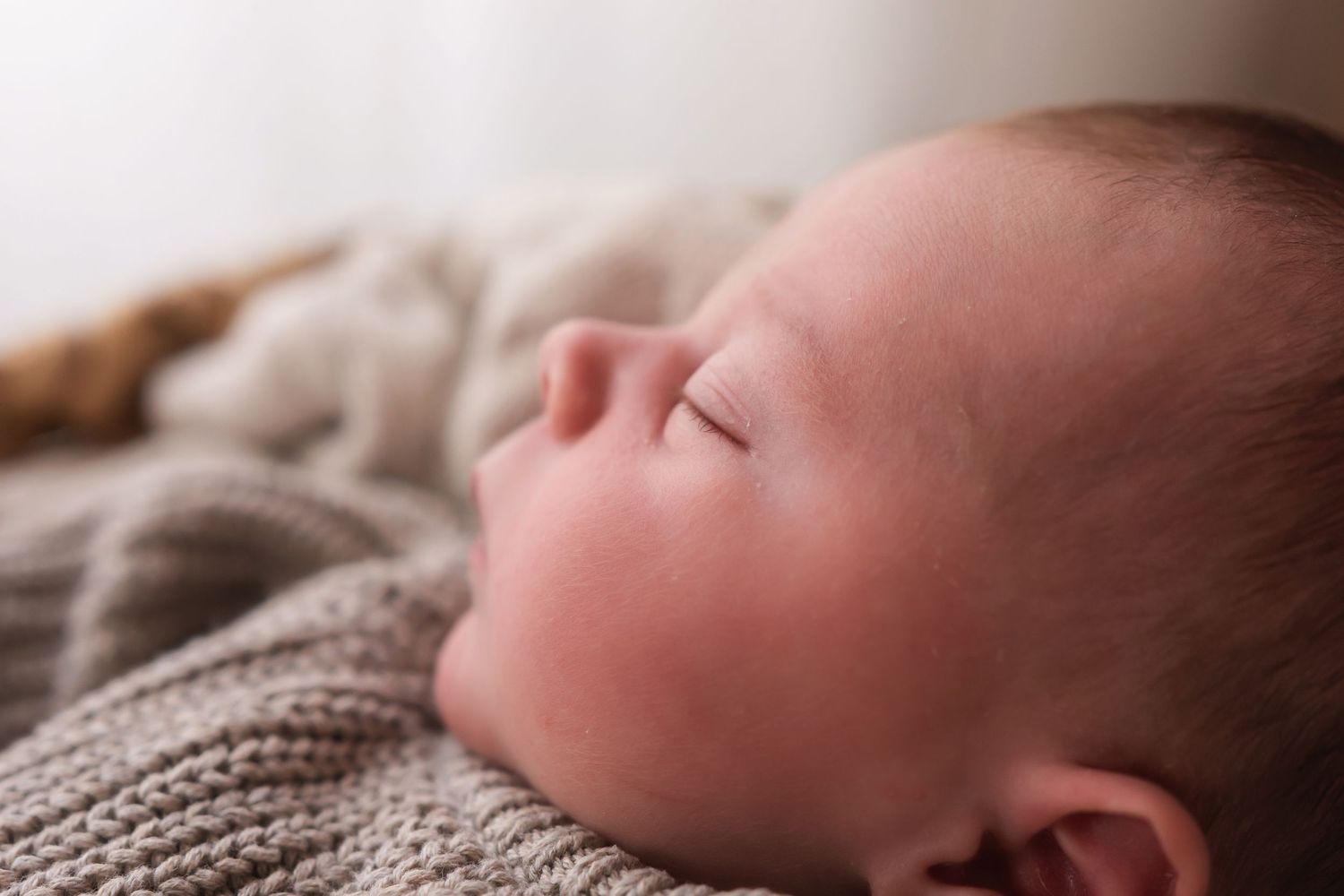 Extreme close-up portrait of a sleeping newborn baby with soft skin resting on a knit blanket.