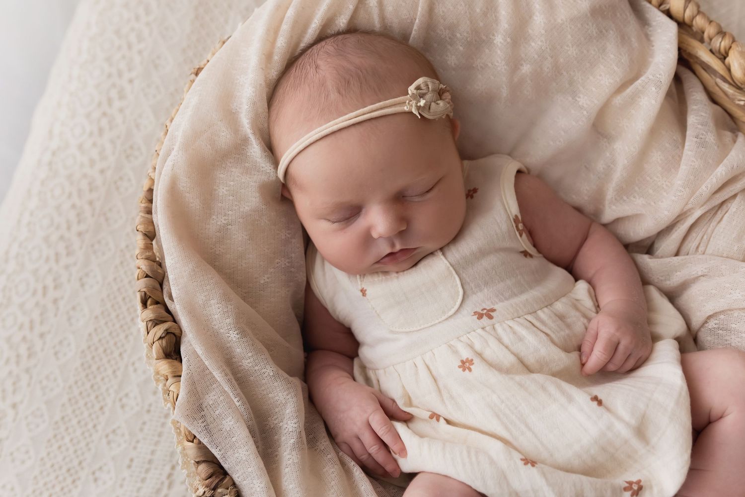Newborn baby girl in cream romper sleeping in wicker basket.