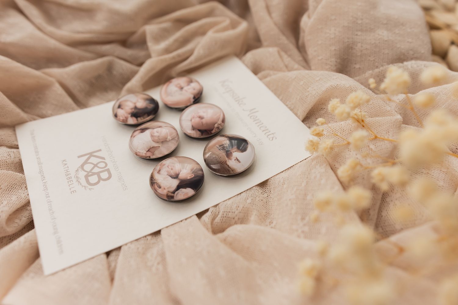 Marble-patterned round buttons displayed on a branded card, surrounded by soft beige fabric and dried flowers.