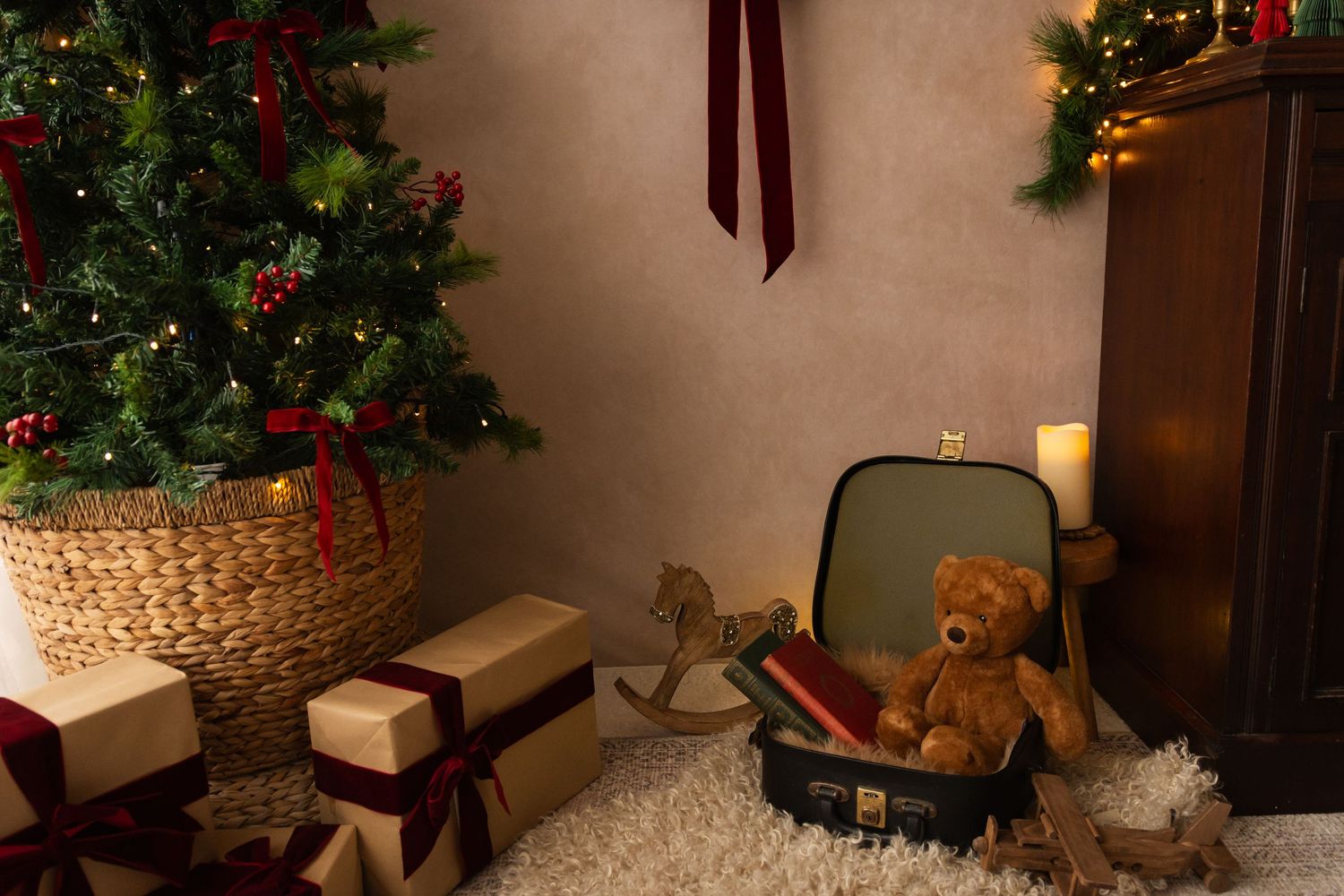 Cozy Christmas scene with decorated tree, wrapped gifts, teddy bear in suitcase, and rocking horse on white fur rug.
