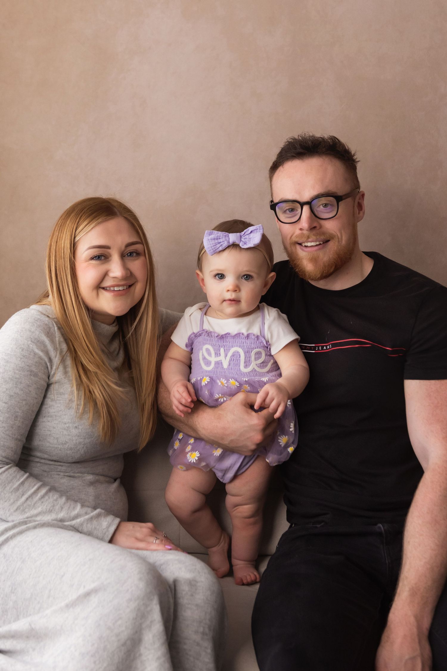 Happy family portrait with parents and baby girl in purple ONE outfit celebrating first birthday.
