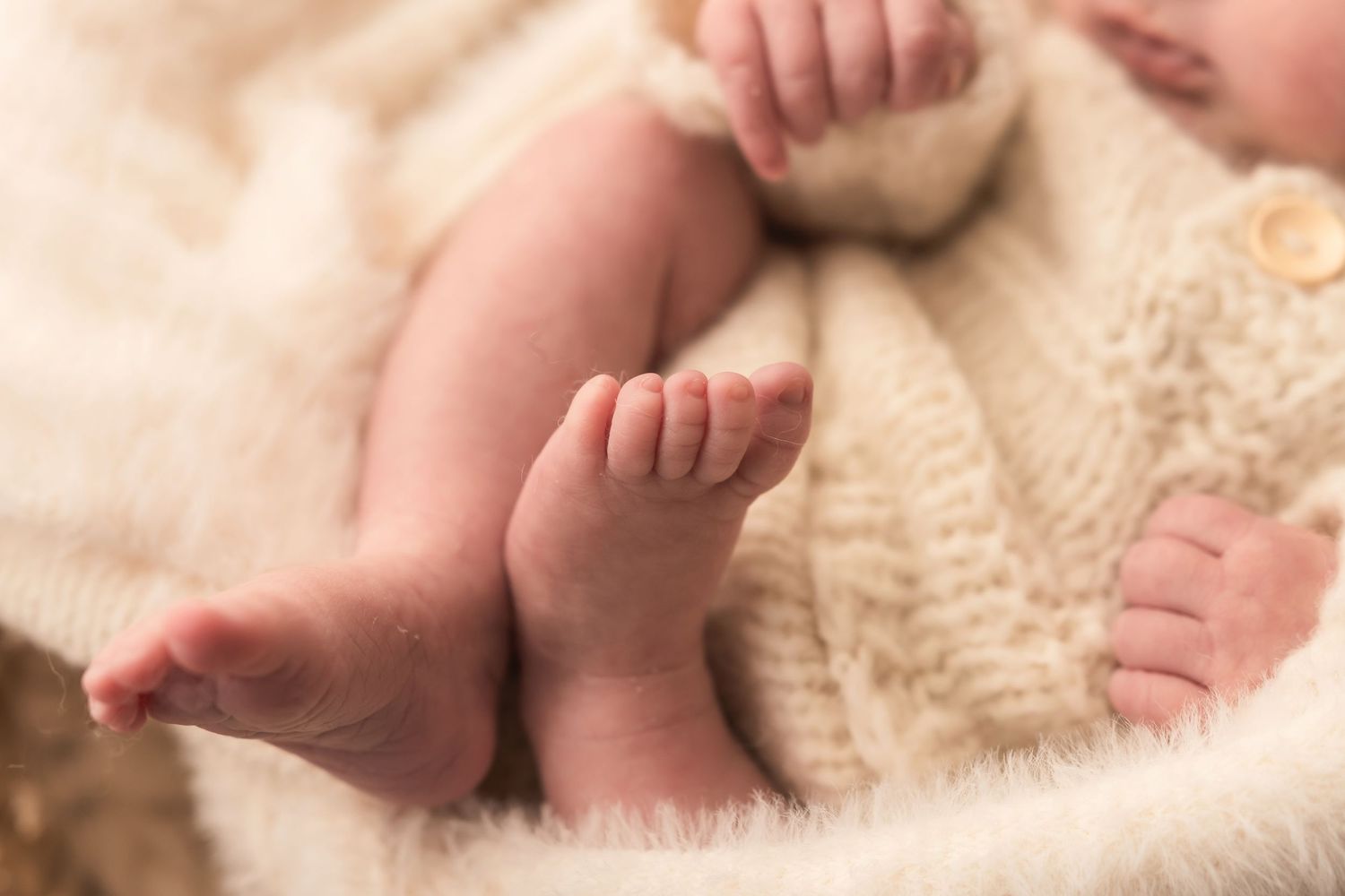 Close-up of tiny newborn baby feet and toes resting on soft white fur blanket.