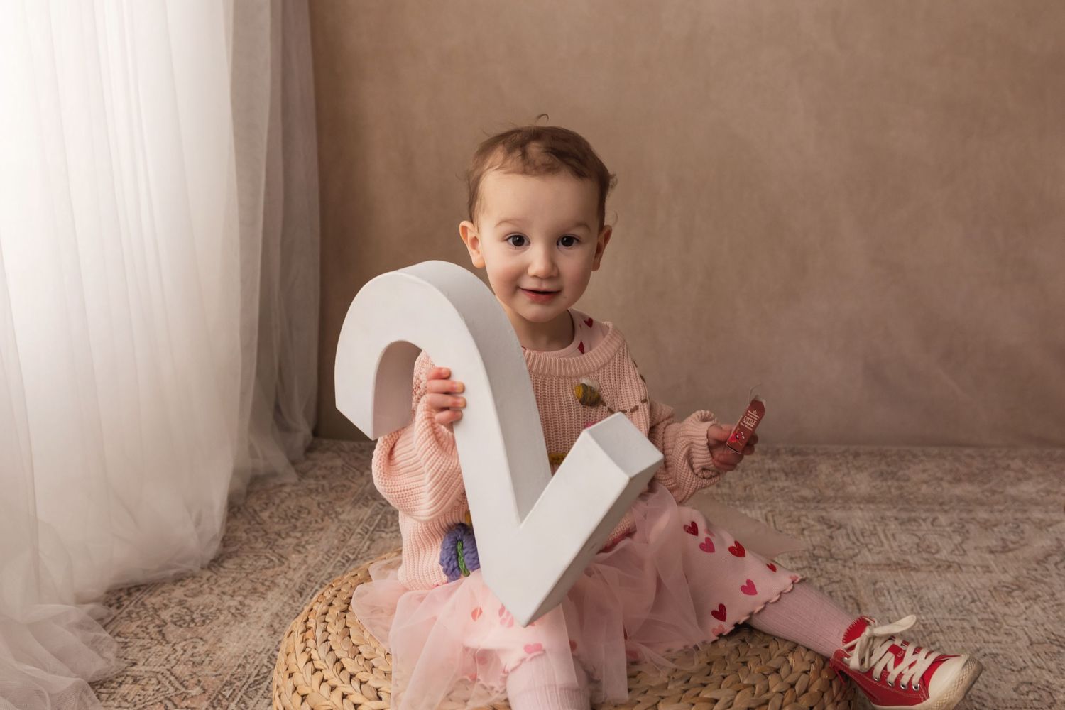 Smiling toddler girl in pink dress holding large number 2 sign for second birthday photo session.