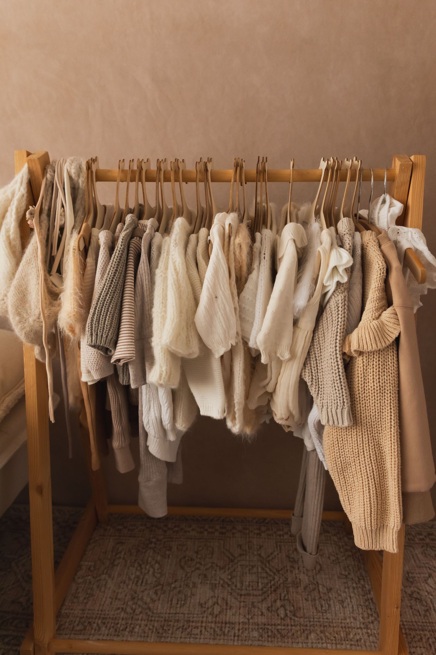 Neutral toned knit sweaters and cozy garments hanging on a wooden clothing rack.