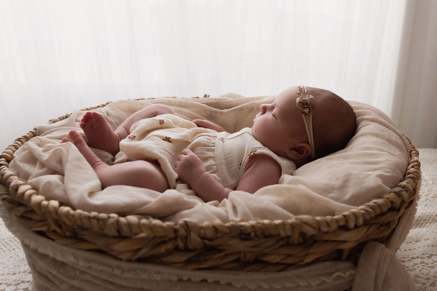 Peaceful newborn baby with headband sleeping in round wicker basket.