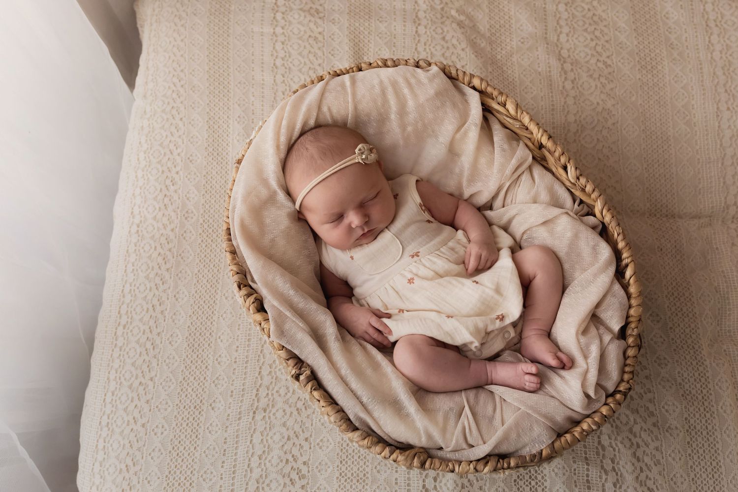 Sleeping newborn baby in cream outfit resting in wicker basket.