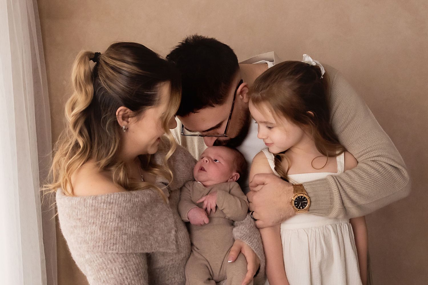 Loving family portrait with mother, father, older daughter, and newborn baby together.