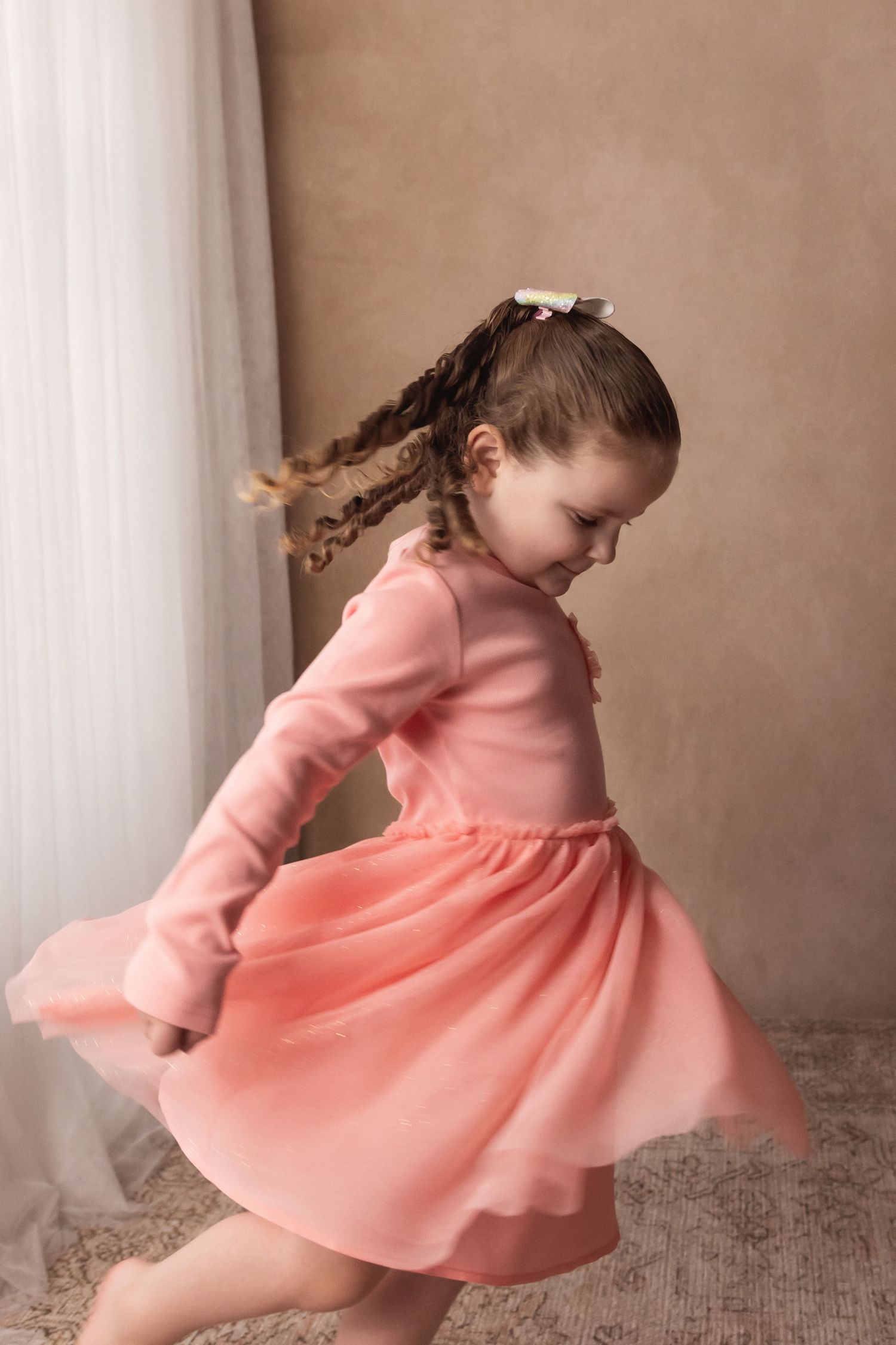 Young girl in pink dress twirling and dancing during a studio birthday portrait photo session.