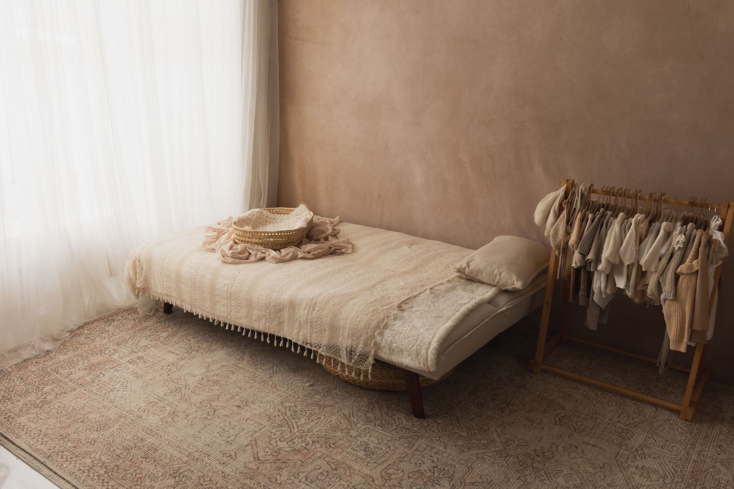 Minimalist newborn photography studio with beige daybed, neutral props, and clothing rack.