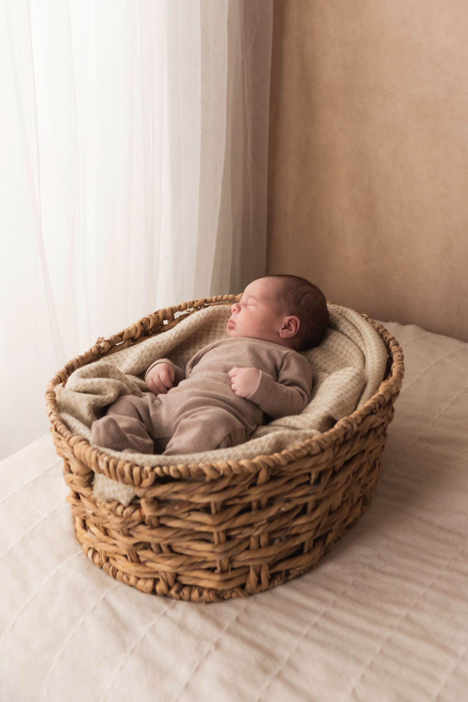 Peaceful newborn baby sleeping in a cozy wicker basket with soft neutral blankets in a studio.