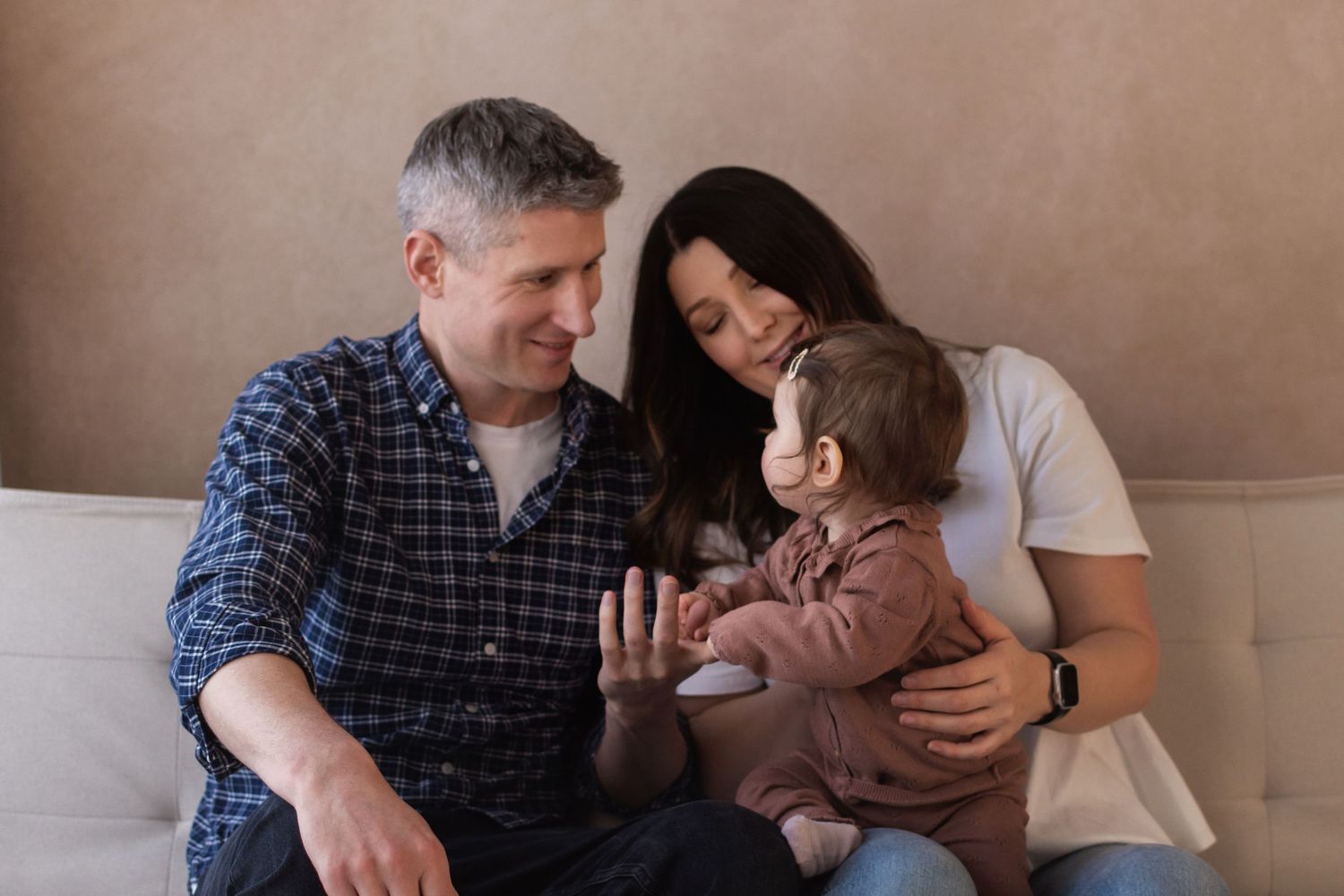 A happy family with a man, woman, and baby sitting together on a couch in a warm, cozy setting.