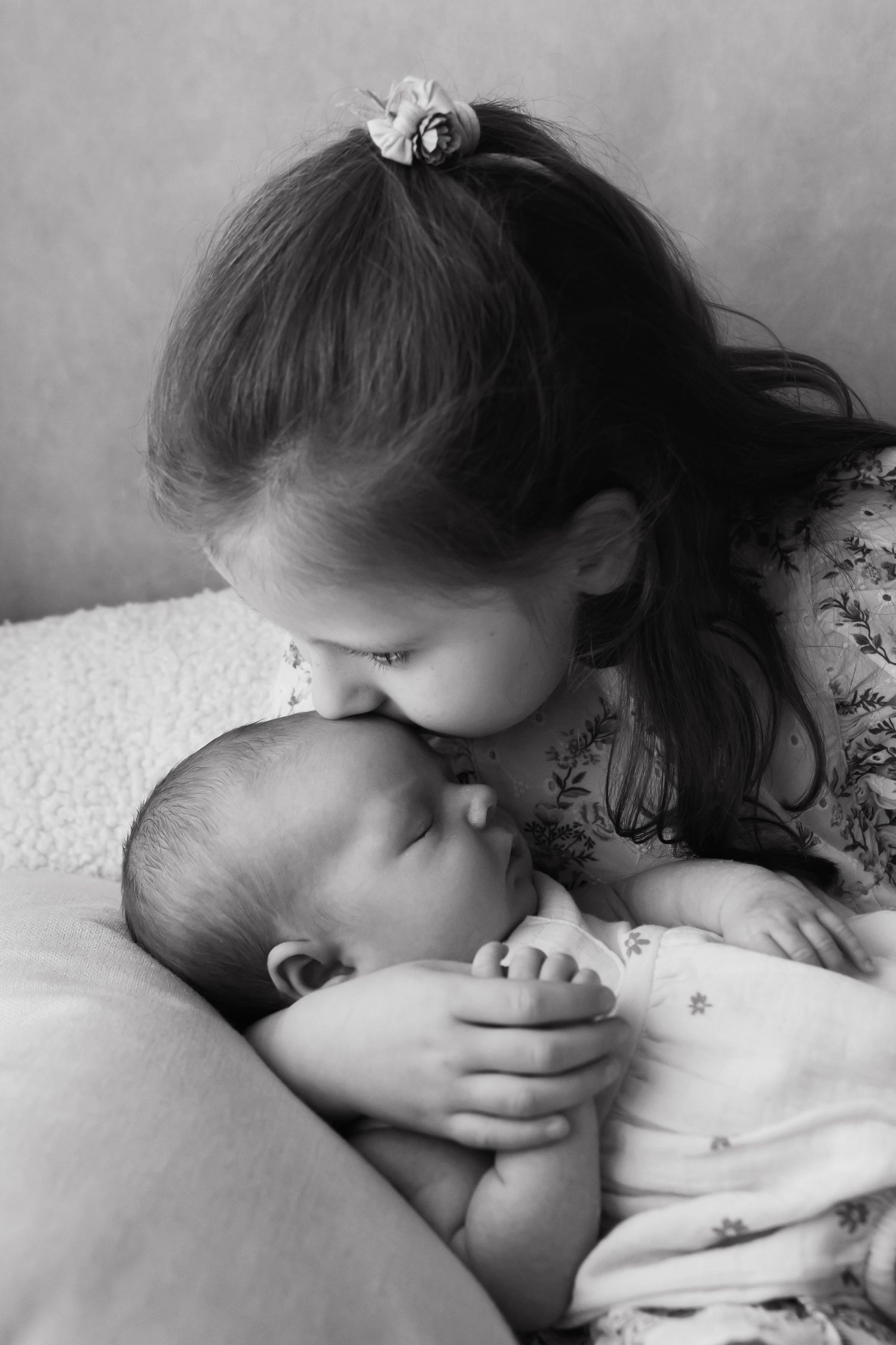 Black and white photo of a young girl tenderly kissing a sleeping newborn baby.