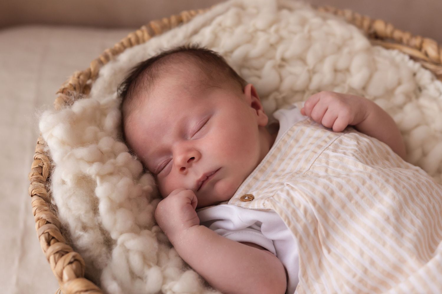 Newborn baby sleeping peacefully in a wicker basket lined with cream wool blanket.