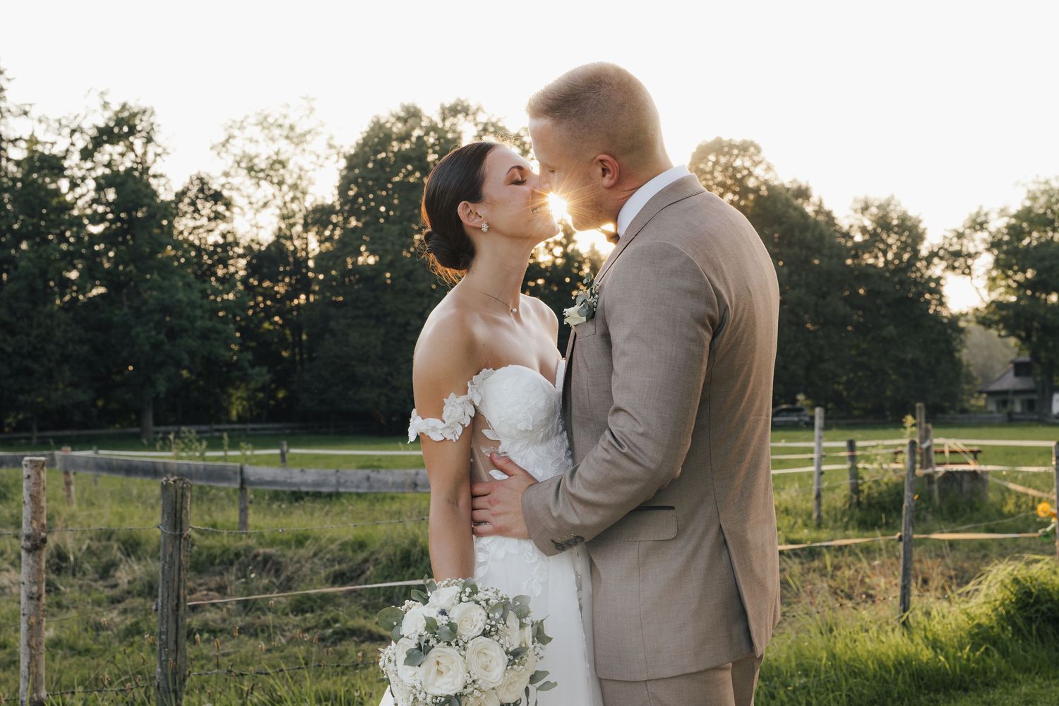 A romantic couple embraces in a sunlit field during golden hour while dressed in wedding attire.