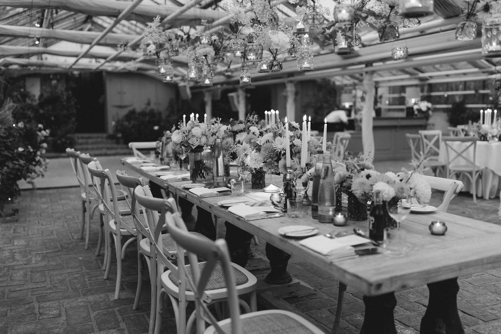 Elegant outdoor wedding reception tables decorated with floral centerpieces and white linens under a covered patio area.