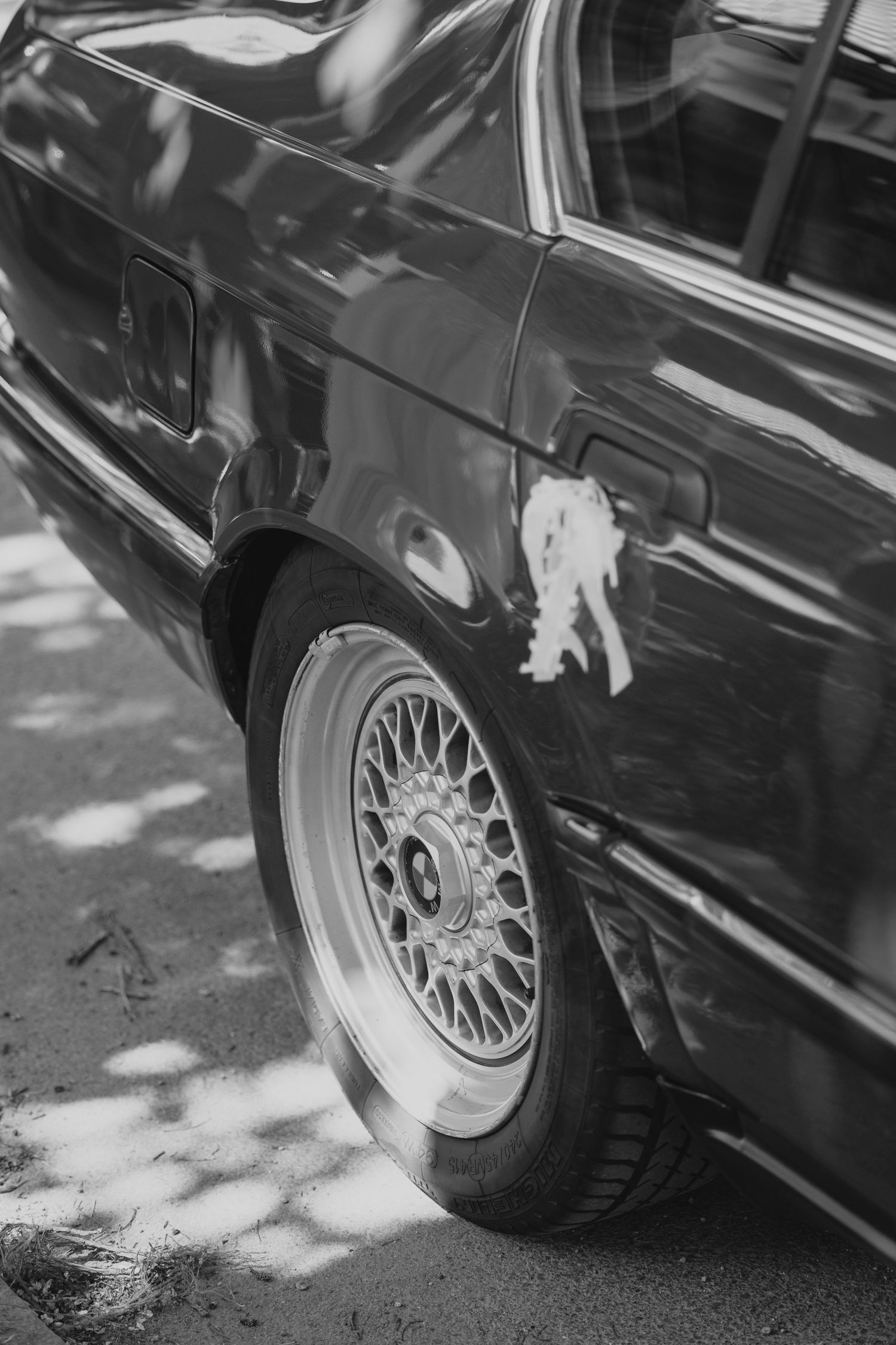Black and white photograph showing a close-up view of classic car wheels with detailed BBS style rims on pavement.