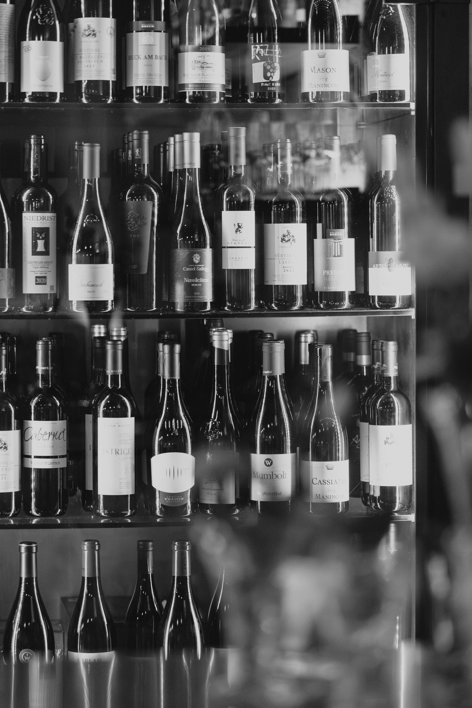 Black and white photograph of wine bottles lined up on shelves in a bar or restaurant display.