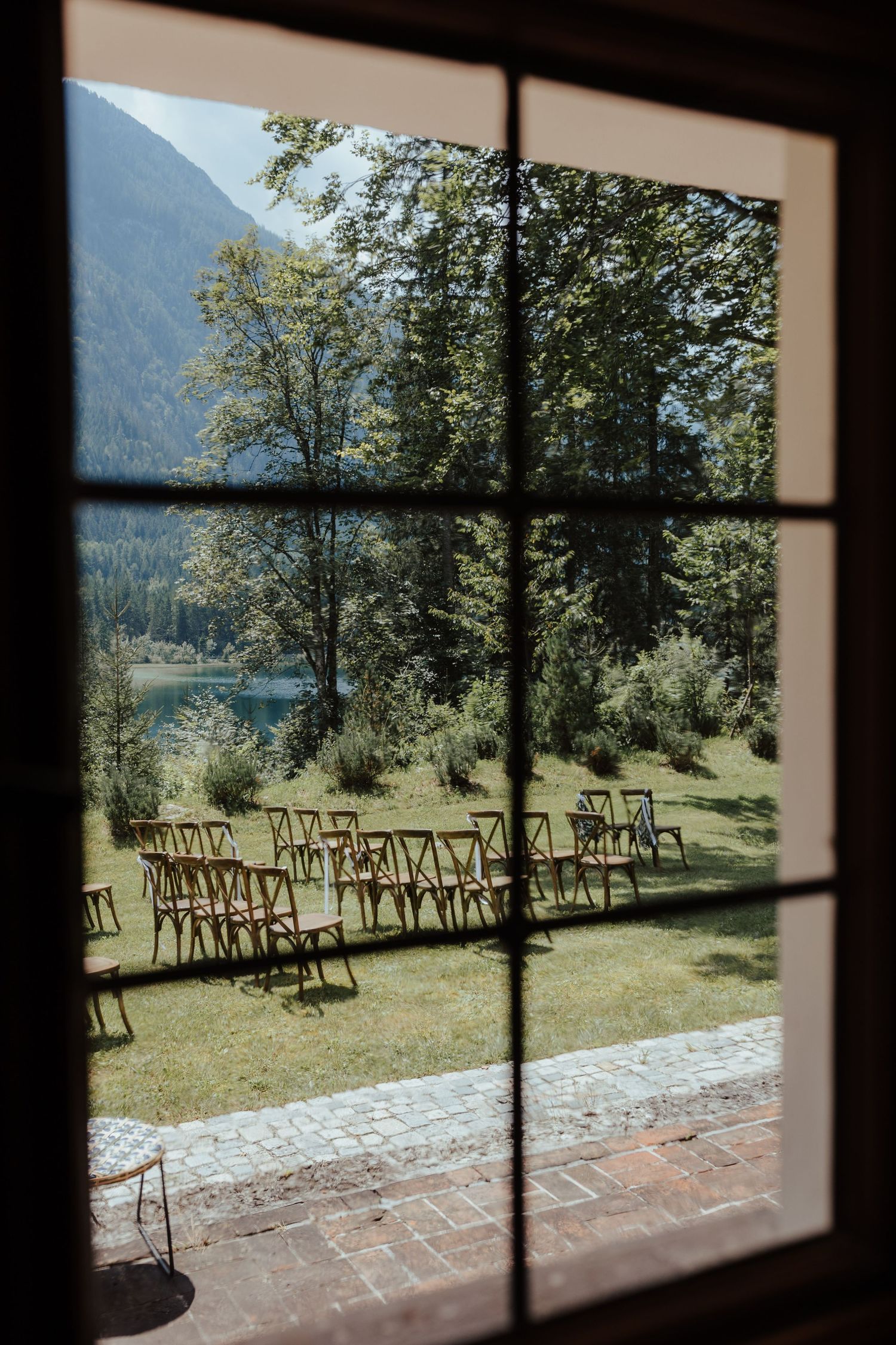 Rows of wooden chairs arranged outdoors for a ceremony with mountain lake and forest views through window panes.