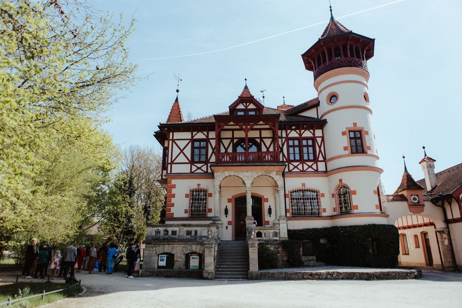 A panoramic view of a historic European-style building complex with red roofs and ornate architecture against a blue sky.