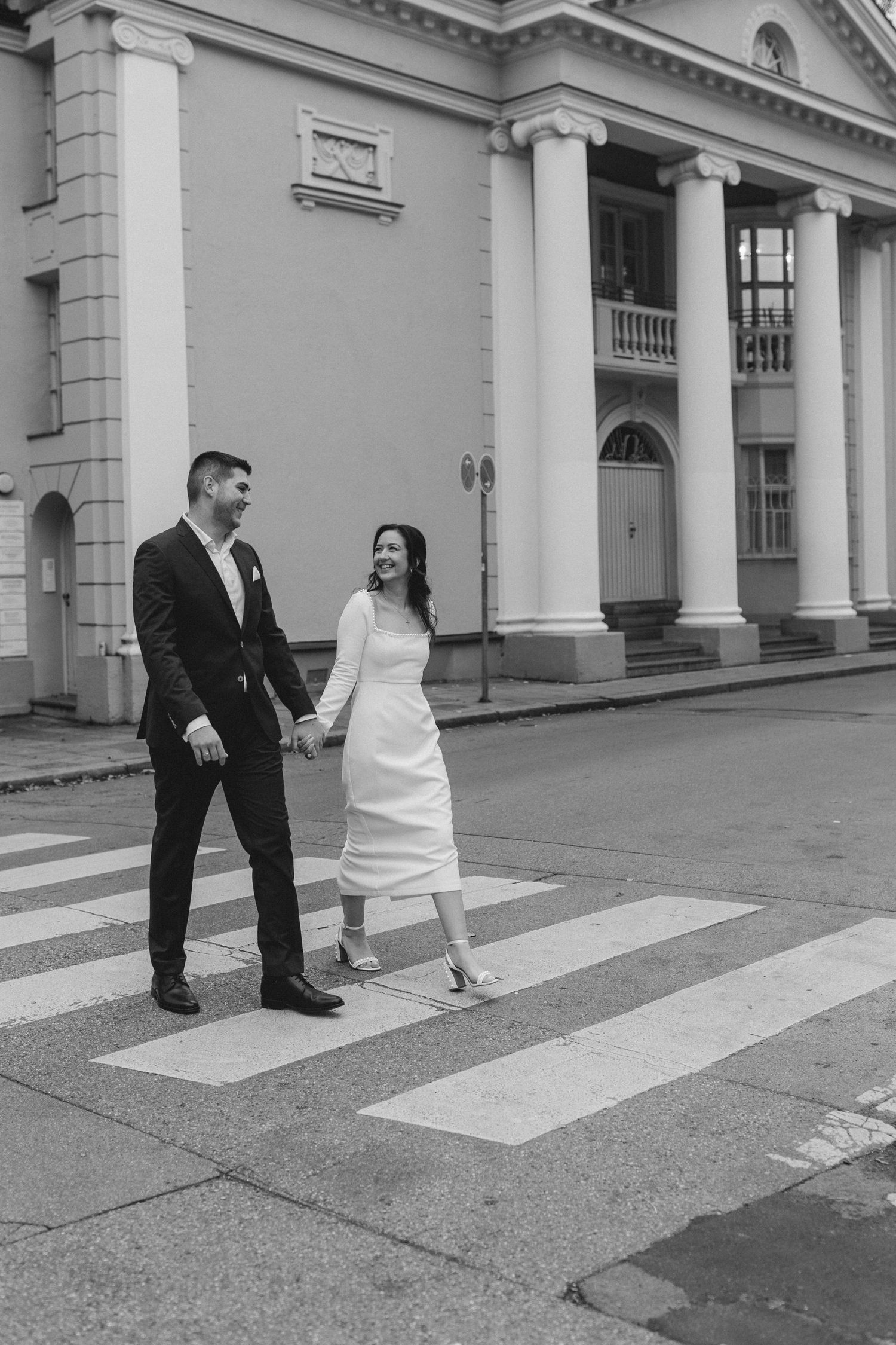 A couple in wedding attire shares a joyful moment together in front of a grand building with white columns.