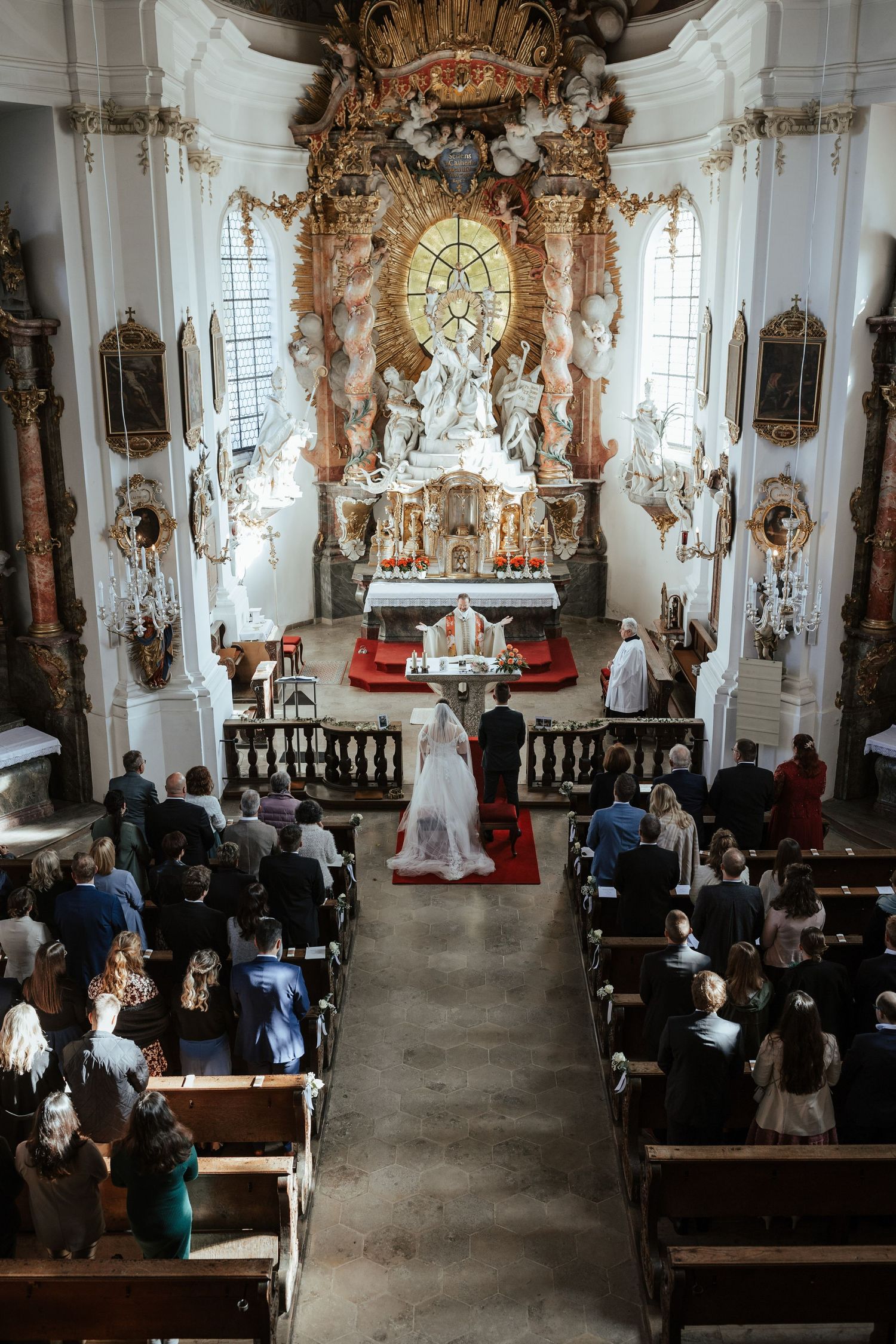 Aerial view of a traditional Catholic church wedding ceremony in an ornate Baroque-style sanctuary with golden altar.