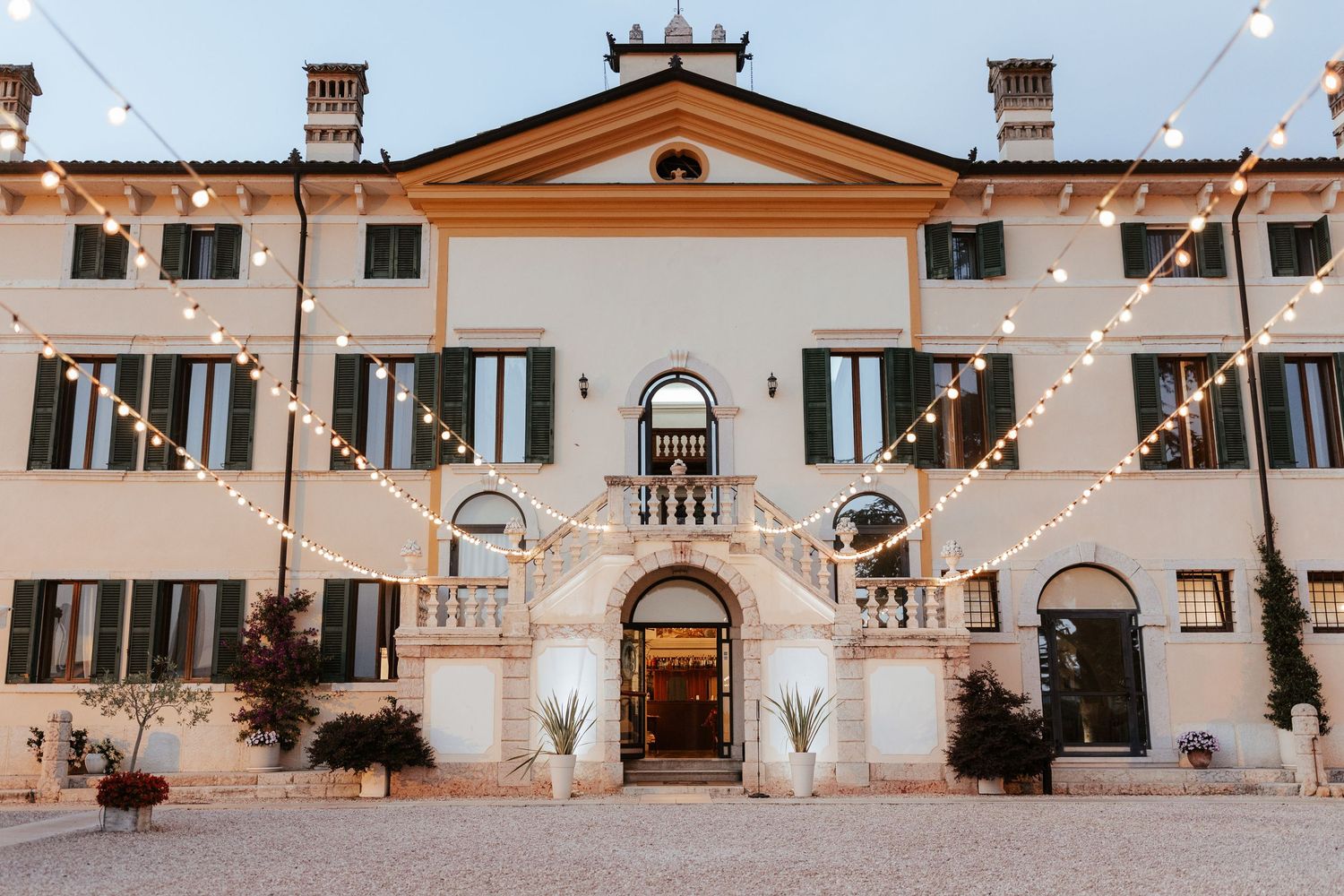 String lights illuminate a rustic Italian villa courtyard with stone walls and traditional architecture at dusk.