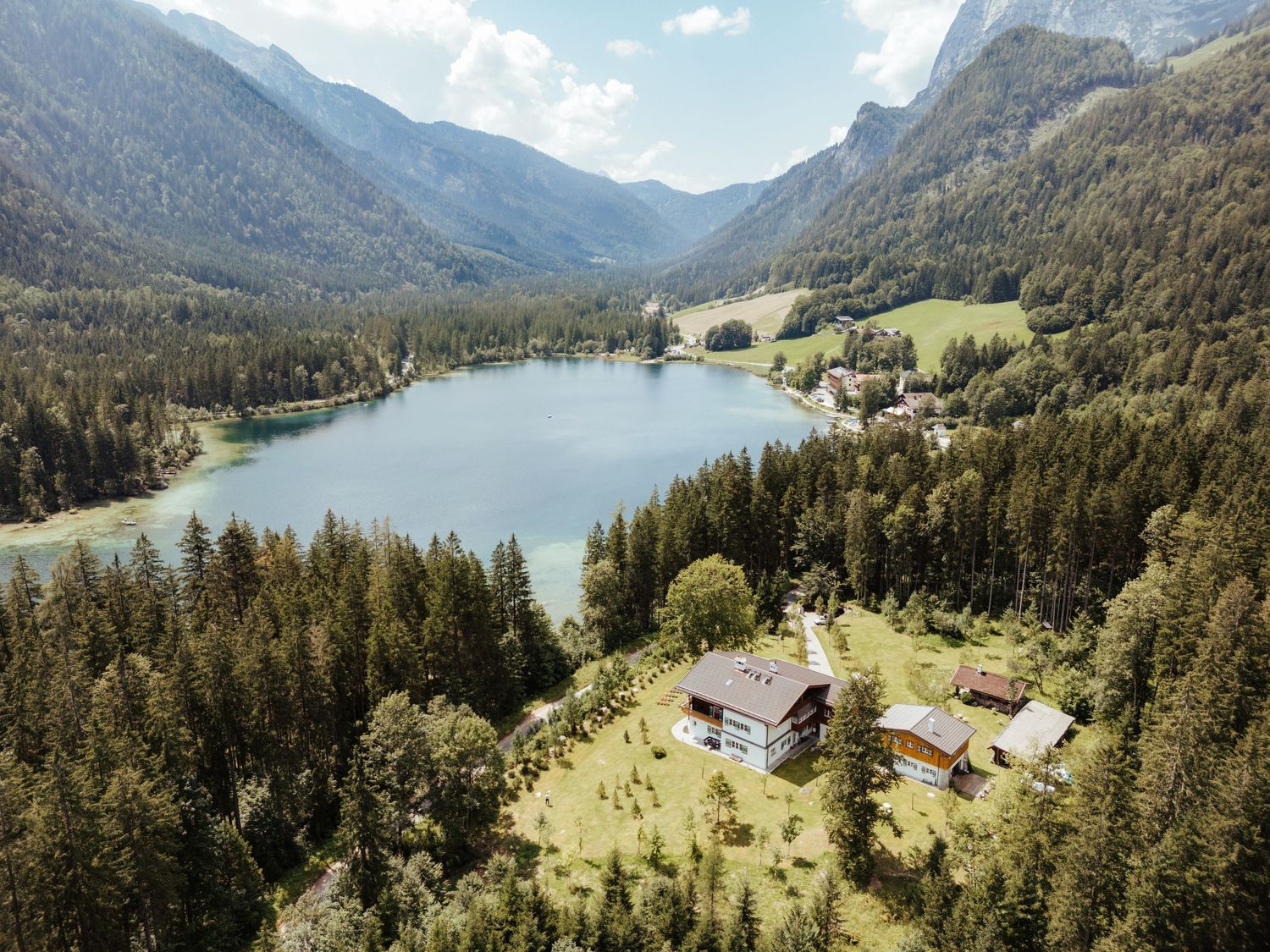 Aerial view of a pristine mountain lake surrounded by forest and alpine peaks with buildings along the shore.