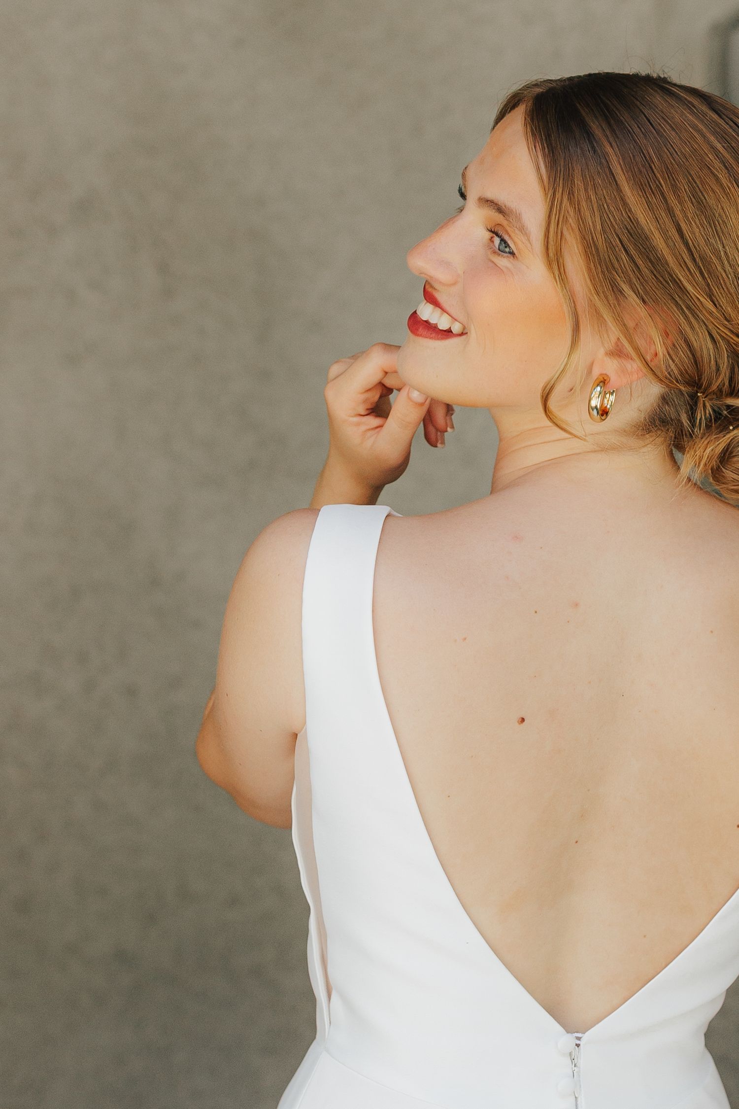 A profile view of someone in an elegant white backless dress with red lipstick and delicate earrings.