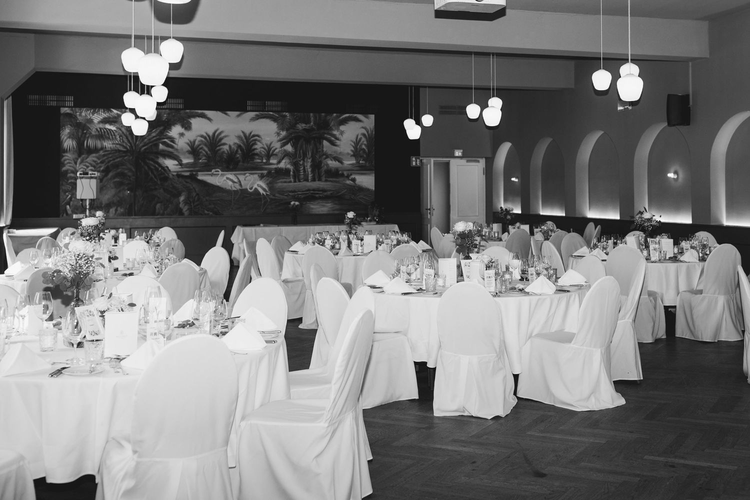 Elegant banquet hall setup with white-clothed tables and hanging light fixtures for a formal event.