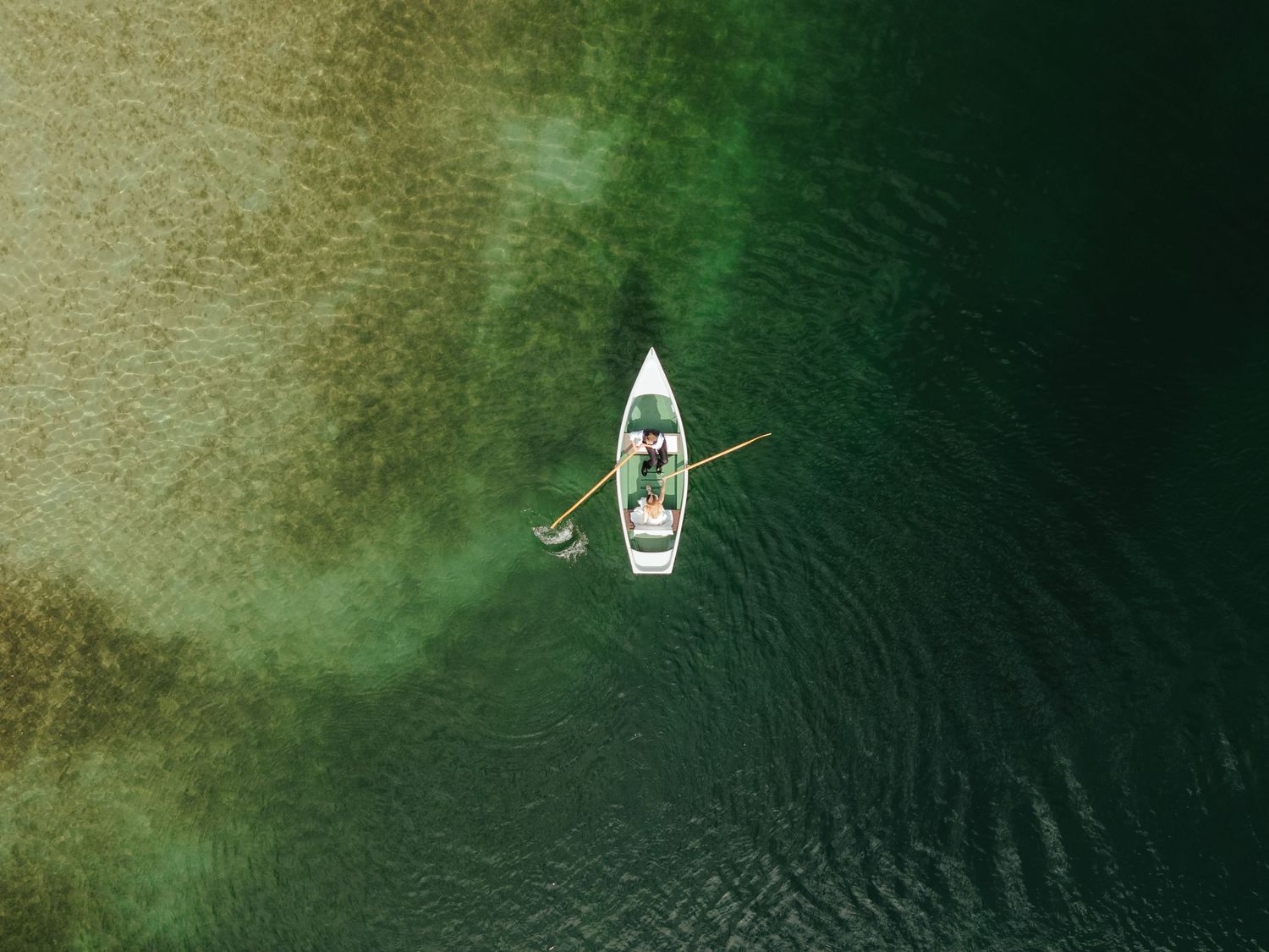 Aerial view of a small boat creating ripples while moving through dark green water.