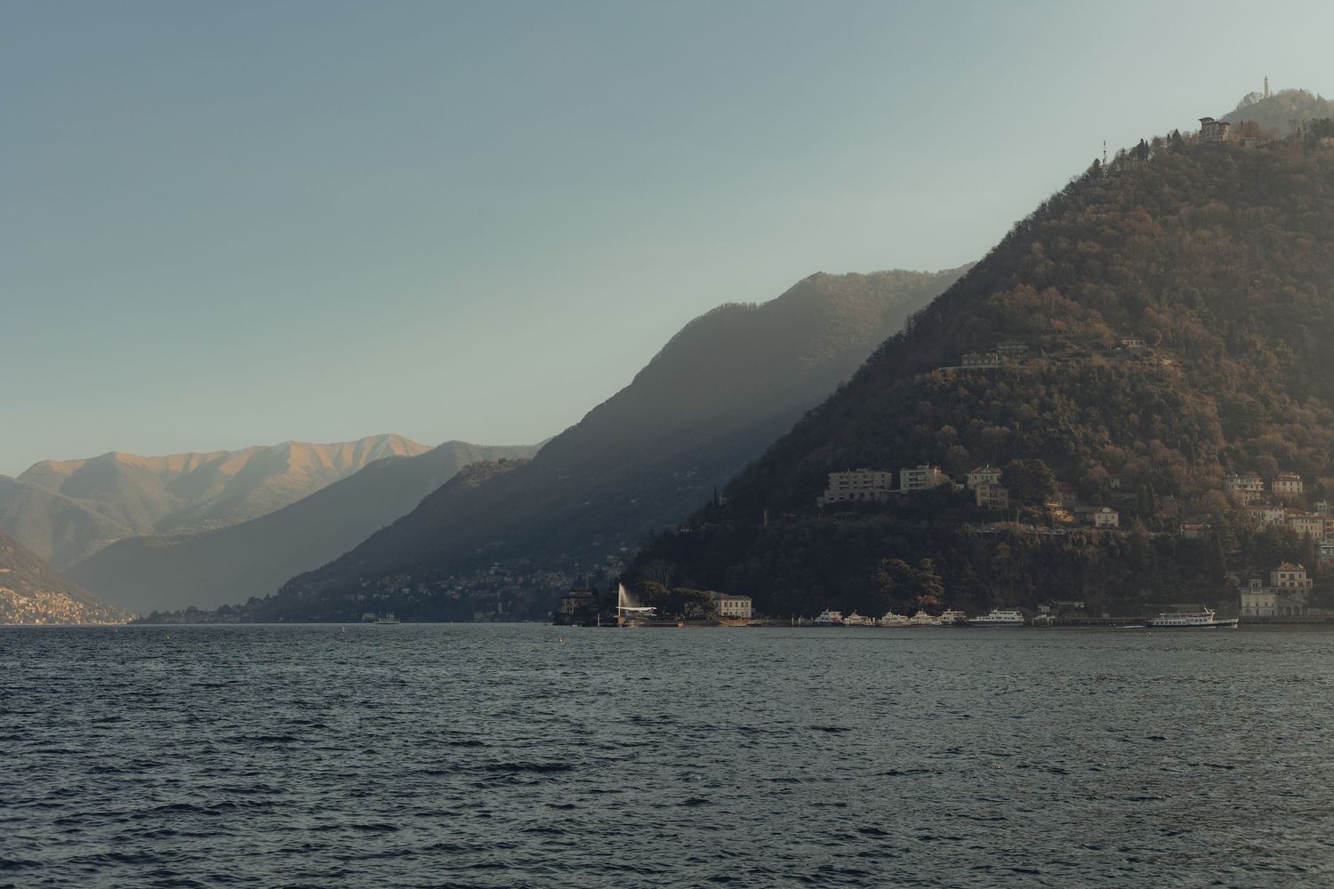 Scenic panoramic view of mountains rising from a misty lake with dramatic cloudy skies in the background.
