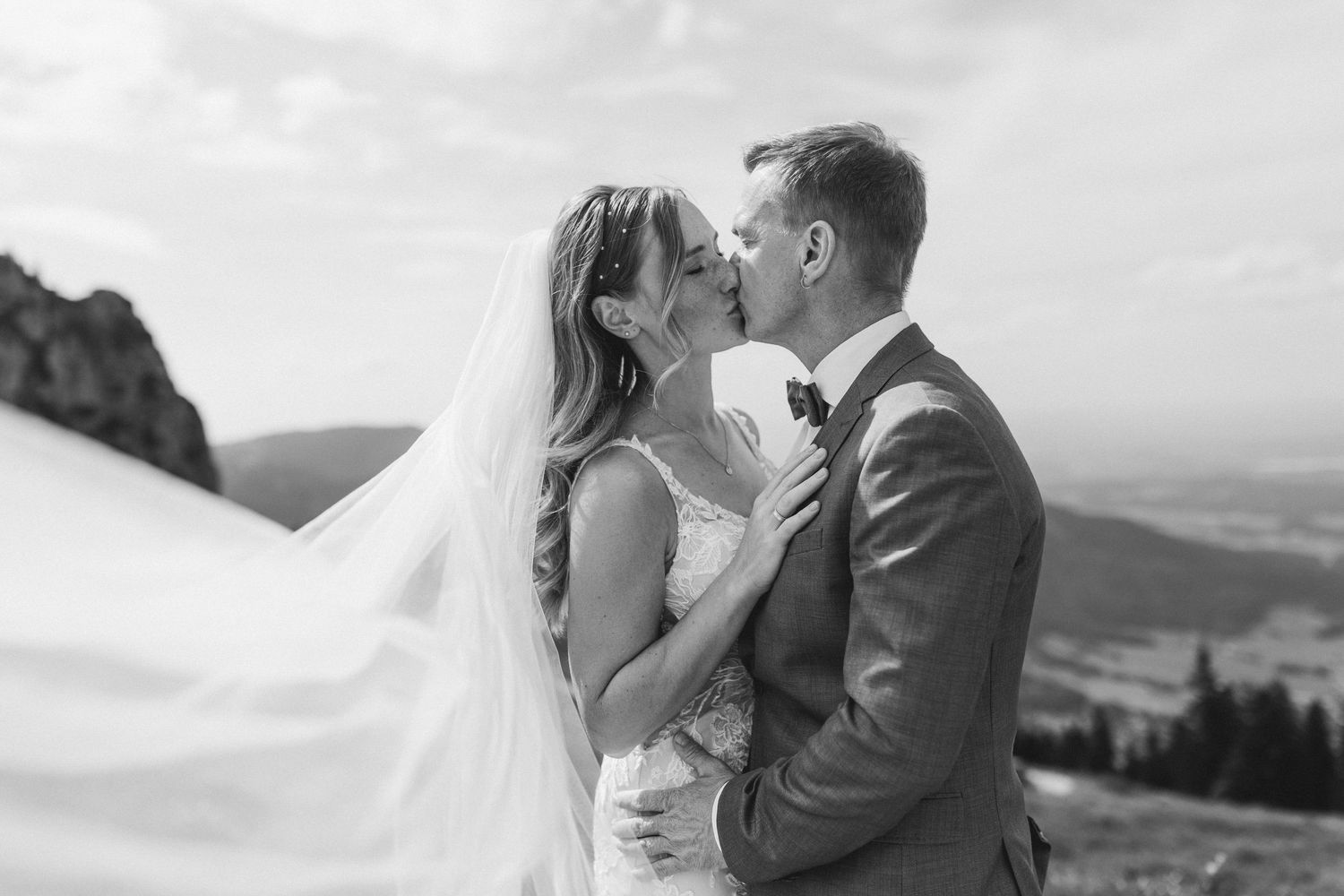 A couple in wedding attire shares romantic kisses in various outdoor settings with mountain and landscape backdrops.