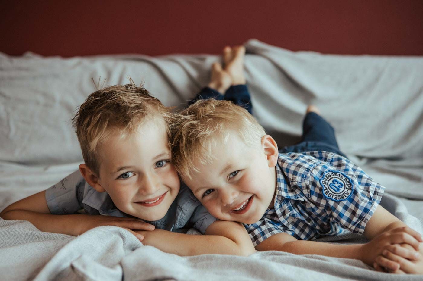 Two young children lying together on white bedding while playing and laughing.