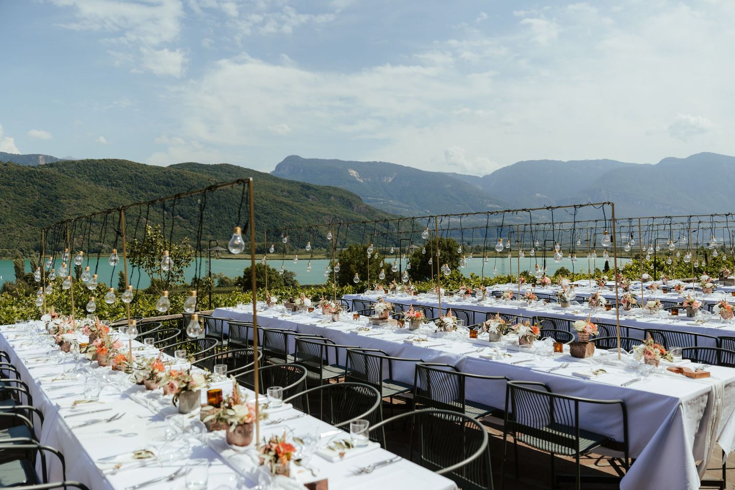 A long banquet table setup outdoors with white linens and floral centerpieces against a backdrop of scenic mountains.