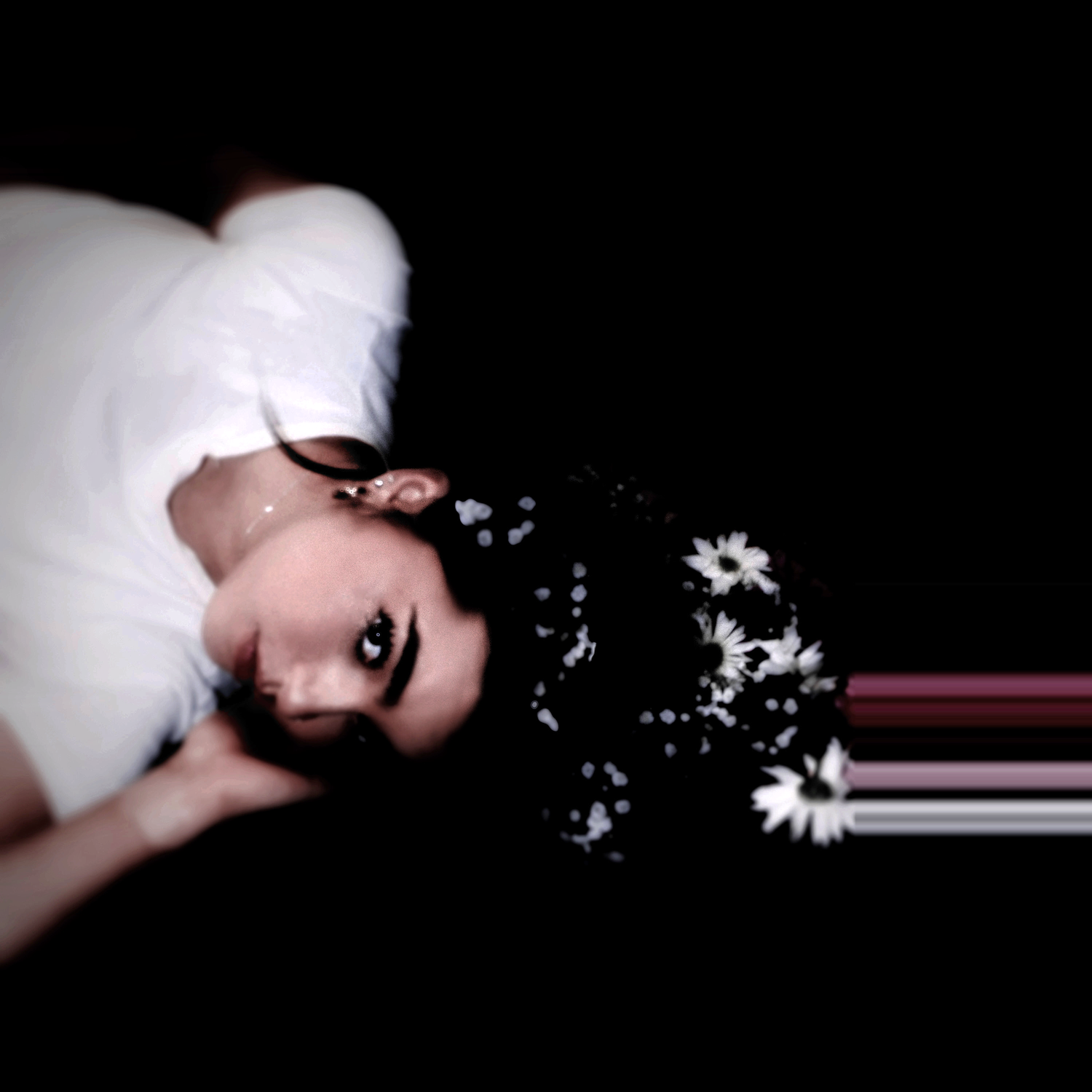 Woman lying down with dark hair adorned with white flowers against black background in artistic portrait.