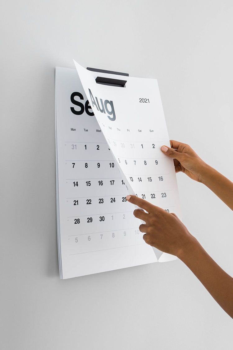Hands pointing to dates on a minimalist white wall calendar for September 2021.