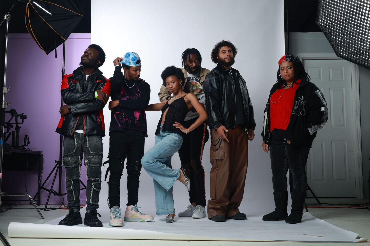 Group of six young adults posing together in a photography studio with professional lighting equipment.